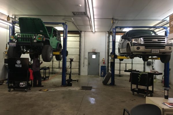 HY-Tech Transmissions inside shop two cars elevated for maintenance. Green jeep on left, ford suv on the right